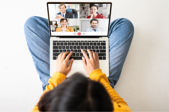 Eine junge Frau sitzt im Schneidersitz
mit ihrem Laptop auf dem Schoß. Auf
dem Bildschirm ist ein virtuelles
Video-Gespräch mit vier Personen zu
erkennen.